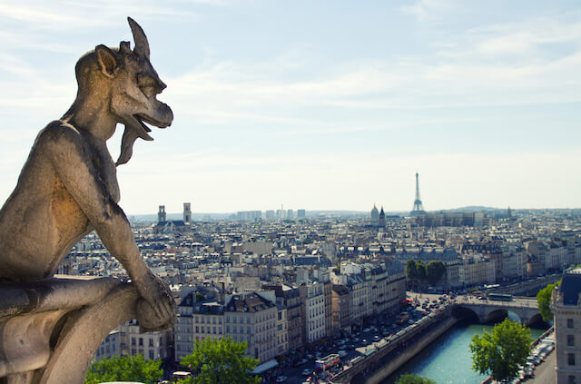 Gargoyle overlooking Paris at Notre Dame Cathedral on a sunny day with the Seine River below and the Eiffel Tower in the distance