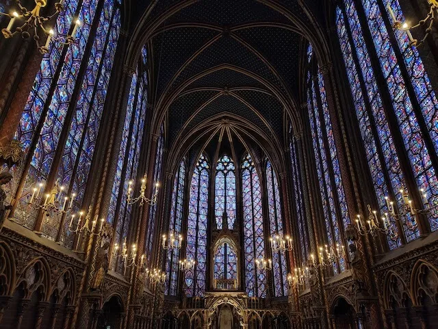 Sainte Chapelle (c) MakeTimeToSeeTheWorld - inside the cathedral surrounded by the stained glass window panes and candelabras lighting along the sides